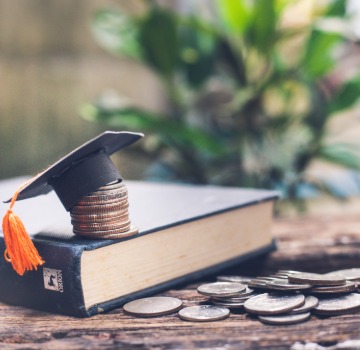 text book on a wooden table with quarters all over it and a stack of quarters piled with a small black graduation cap on it and yellow tassle